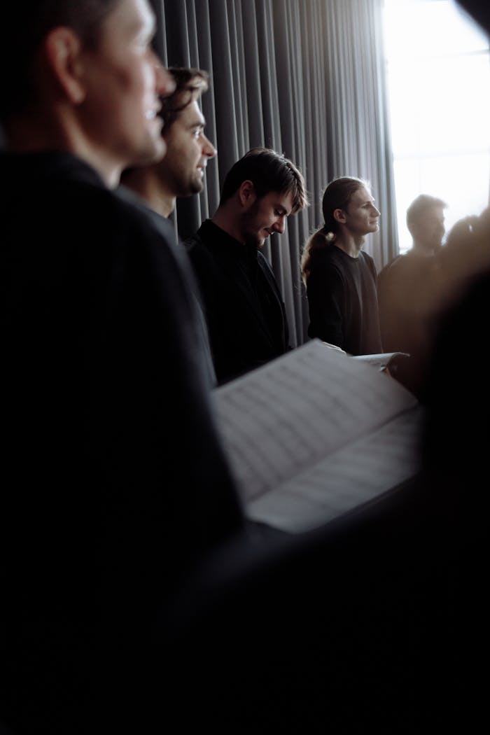 A group of men singing in choir, holding music sheets, indoors.